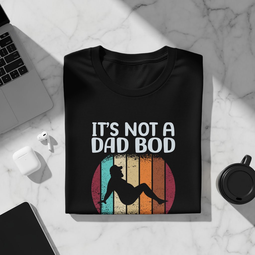 Black t-shirt with "IT'S NOT A DAD BOD" text and a silhouette against a retro sunset graphic.