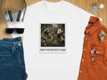 White t-shirt with a polaroid photo of a raccoon and possum sitting on a bench, text reads "Best Friends Don't Judge."