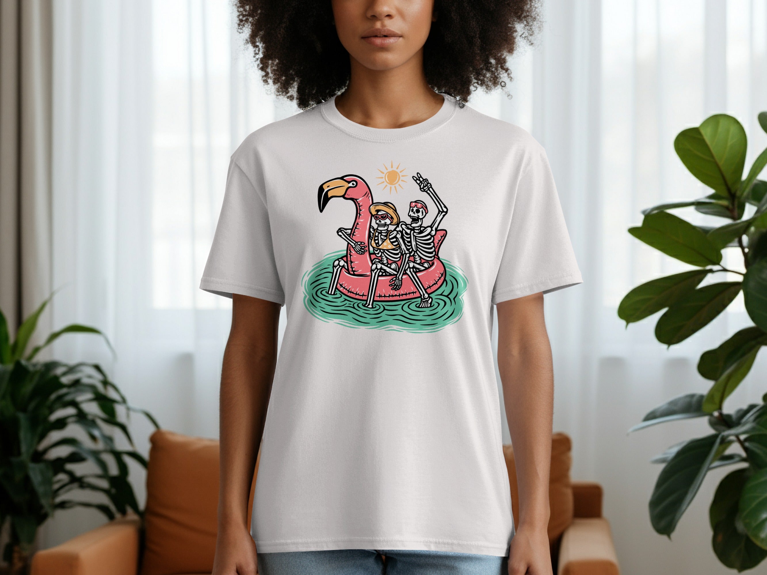 T-shirt graphic of two skeletons riding a pink flamingo float under the sun.
