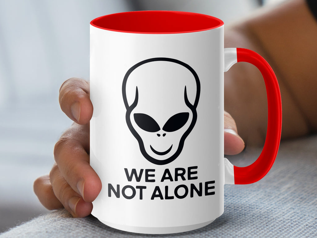White mug with red handle and rim, featuring an alien head and "WE ARE NOT ALONE" text.