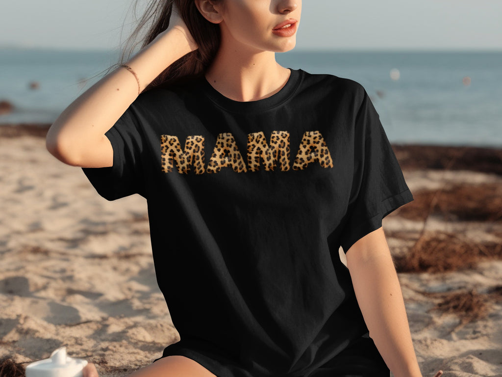 Black t-shirt with "MAMA" in leopard print letters on beach background.