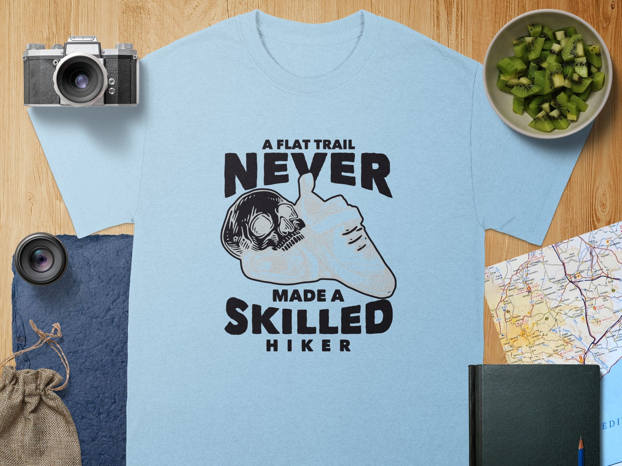 Light blue t-shirt with text "A FLAT TRAIL NEVER MADE A SKILLED HIKER" and skull graphic.
