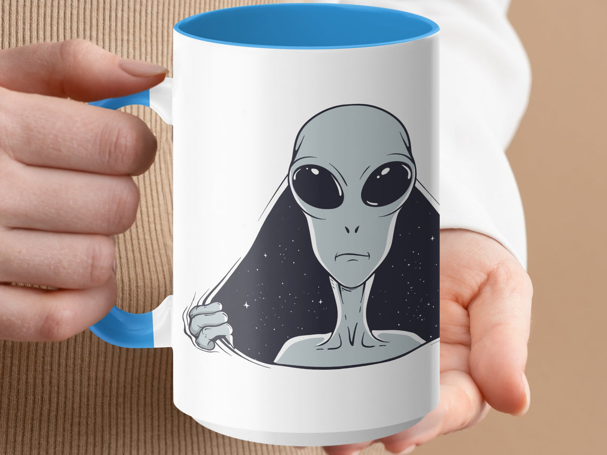 White mug with blue handle features a gray alien head emerging from a starry background.