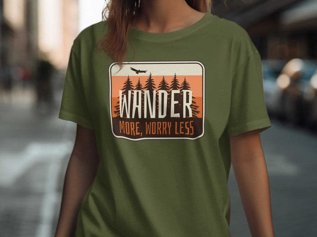 Green t-shirt with a badge graphic featuring pine trees, a bird, and text "WANDER MORE, WORRY LESS".