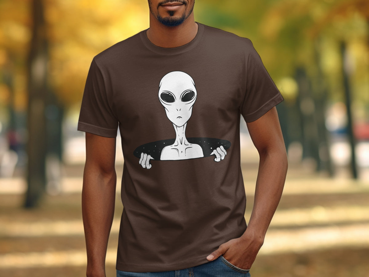 Brown t-shirt with a graphic of a white alien peeking out from a dark oval.