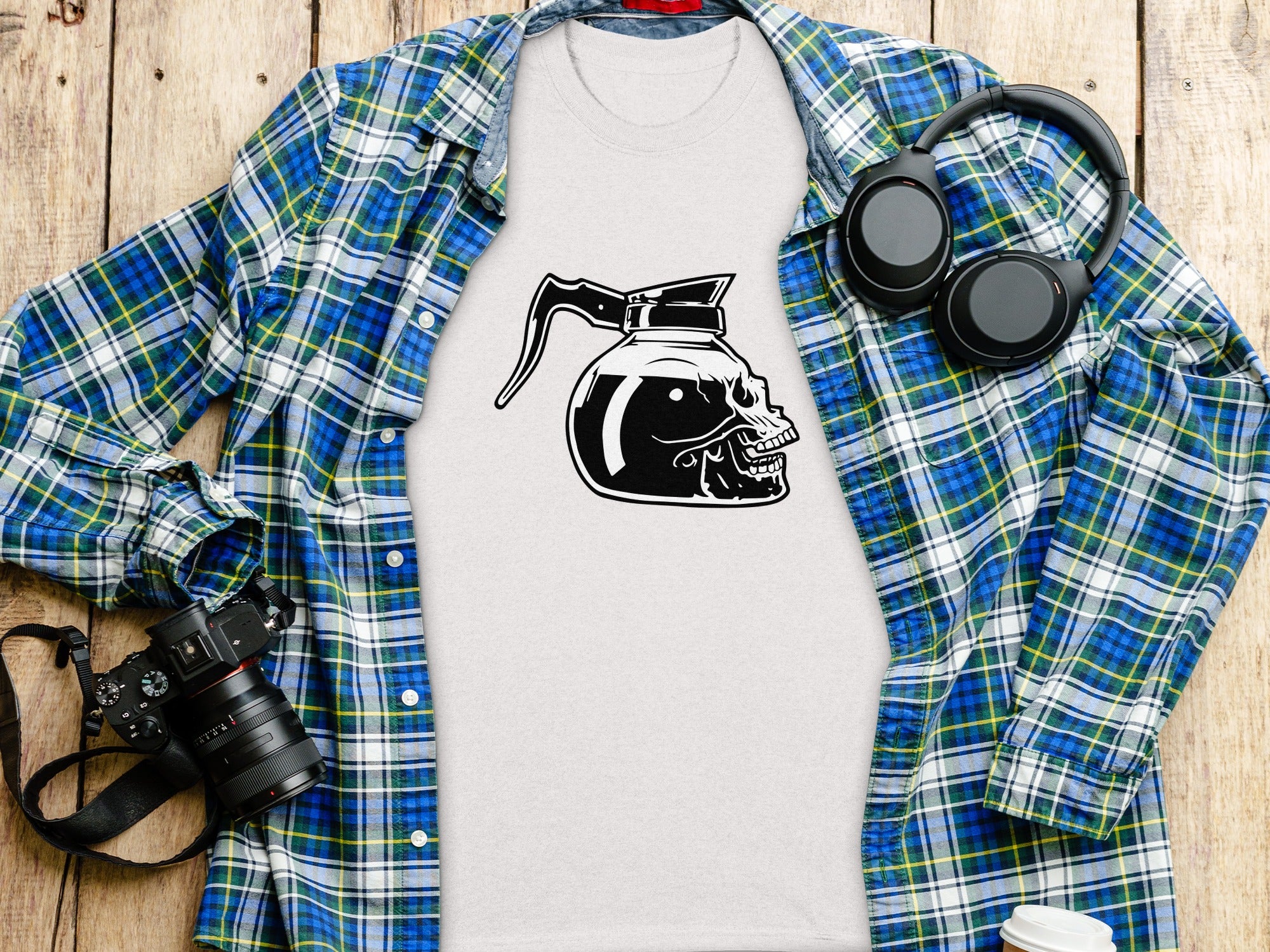 White t-shirt with skull coffee pot graphic, blue plaid shirt, headphones, camera.