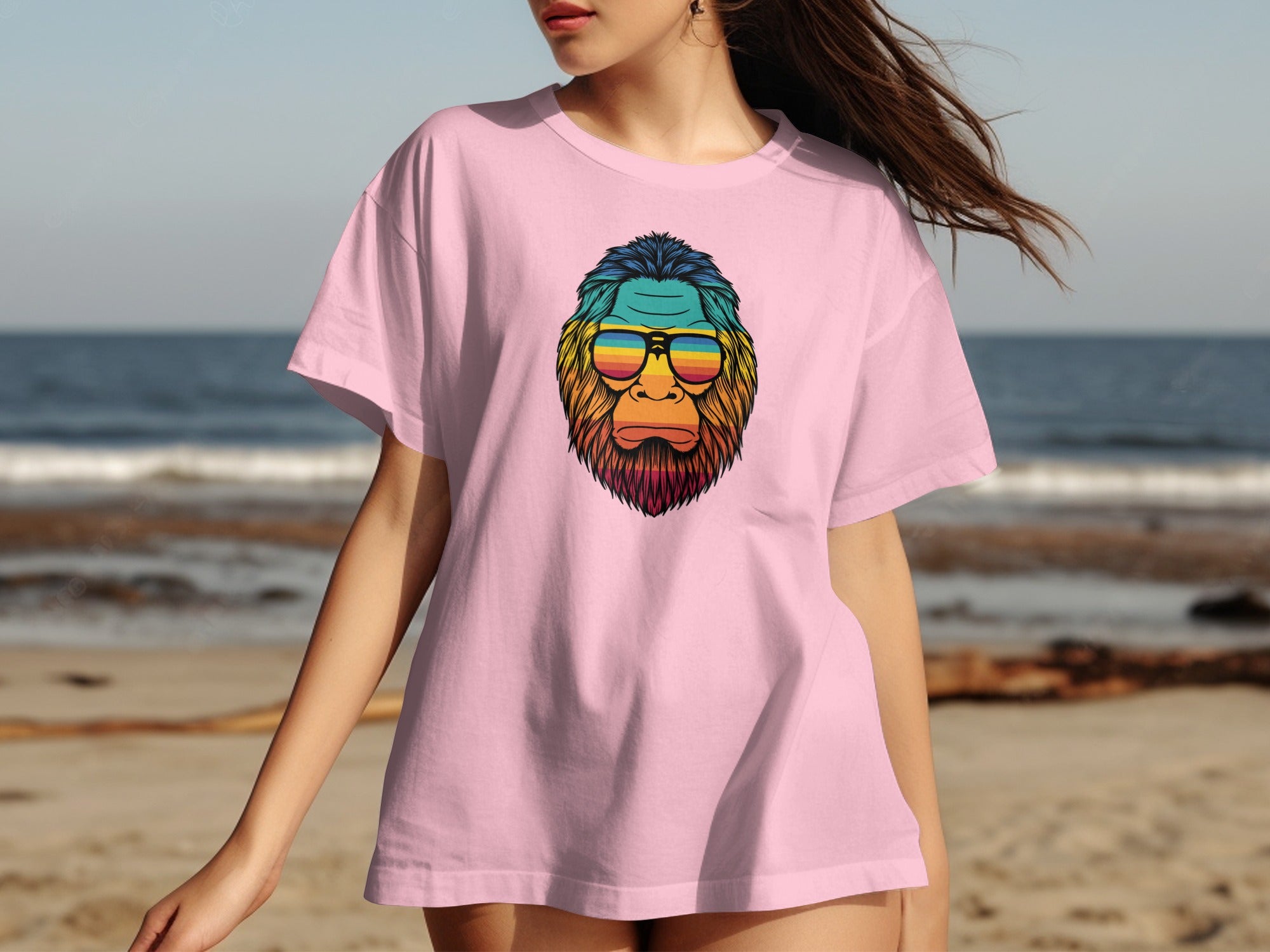 Pink t-shirt with Bigfoot graphic wearing rainbow sunglasses at the beach.