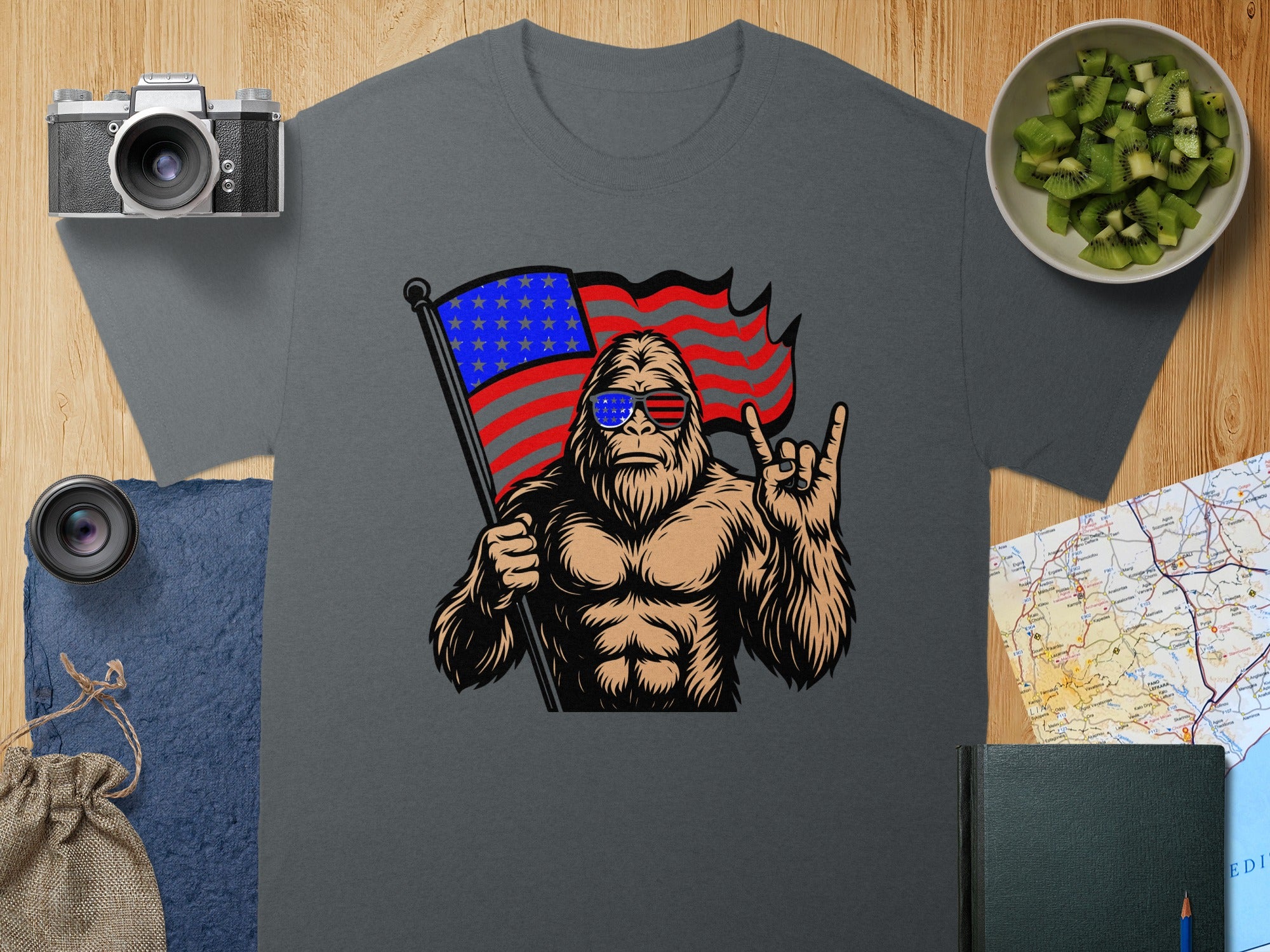 Bigfoot wearing American flag sunglasses holds a flag, giving a rock-on hand gesture.