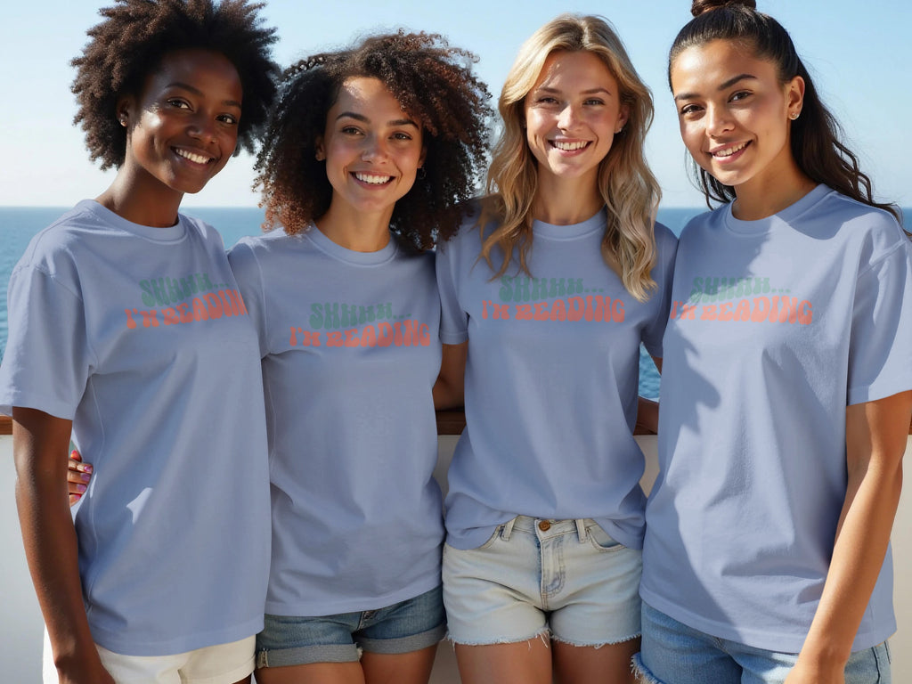 Four young women in matching shirts smiling with the ocean in the background.
