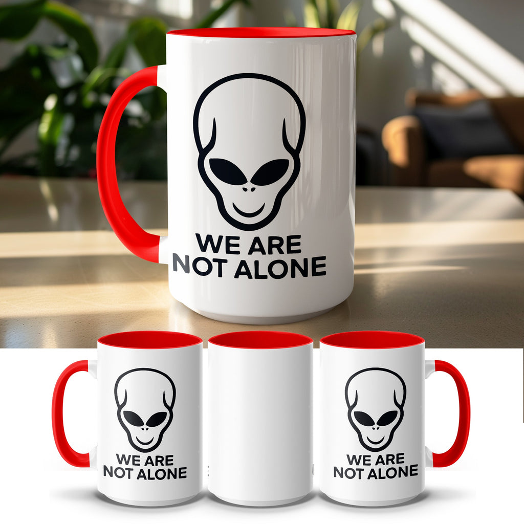 White mug with red rim and handle featuring a black alien head and "WE ARE NOT ALONE" text.