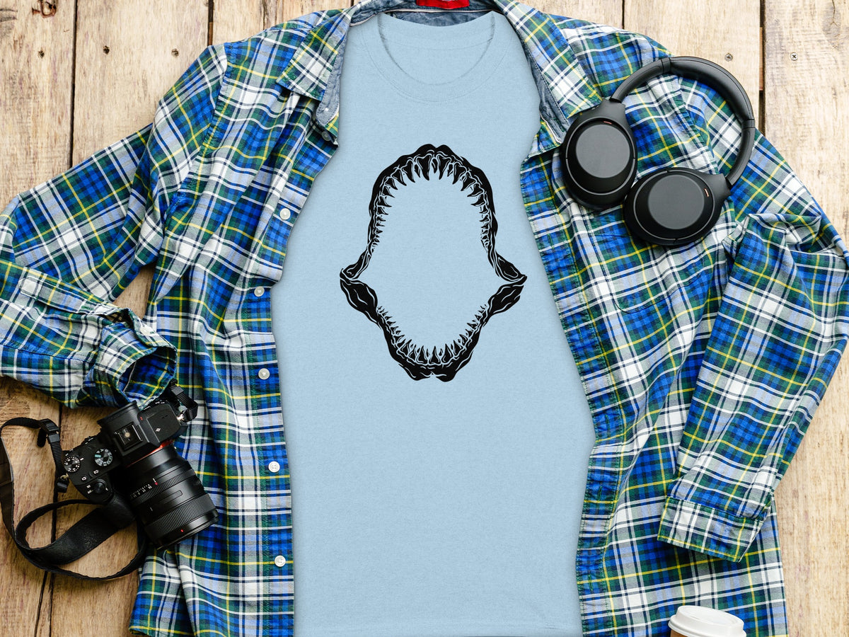 Light blue t-shirt with black shark jaw graphic, plaid shirt, headphones, and camera.