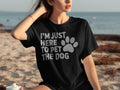 Black t-shirt with white text "I'M JUST HERE TO PET THE DOG" and a paw print.
