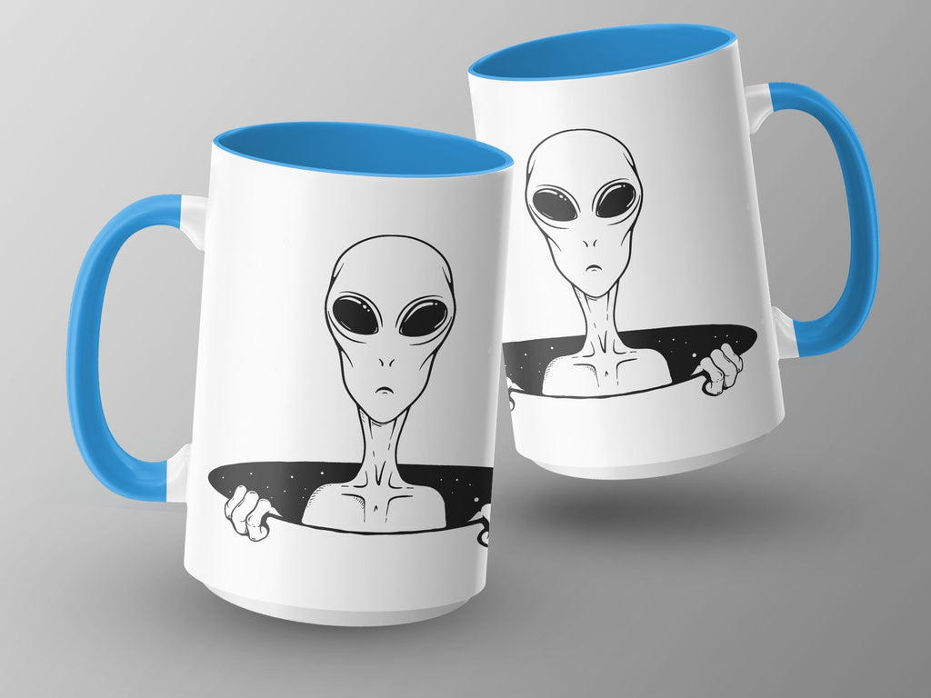 Two white mugs with blue handles featuring black line art of a sad alien peeking out.