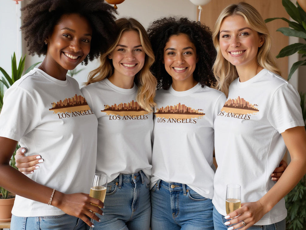 Four women in white t-shirts with a "Los Angeles" skyline graphic, holding champagne.