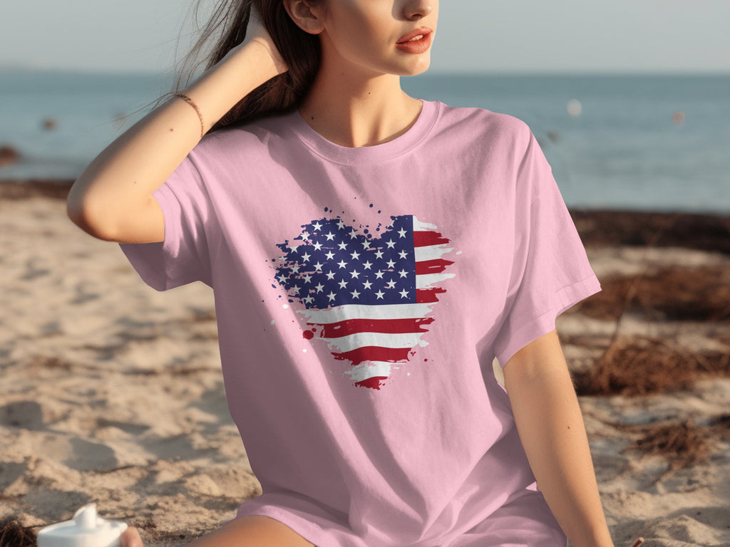 Pink t-shirt with distressed American flag heart design on a beach.