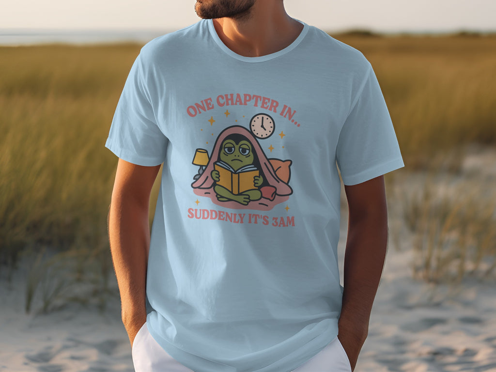 Light blue t-shirt with a graphic of a frog reading a book, "One Chapter In..." and "Suddenly It's 3AM".