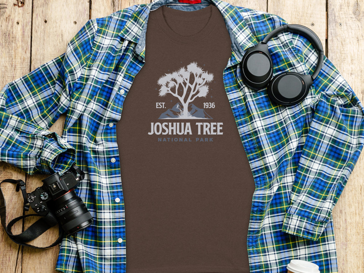 Brown t-shirt with Joshua Tree National Park graphic, laid on wooden surface with flannel shirt and headphones.