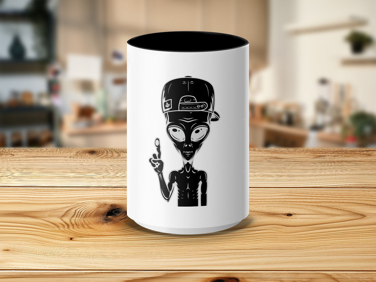 White mug with black interior and a black graphic of an alien wearing a baseball cap and giving peace sign.
