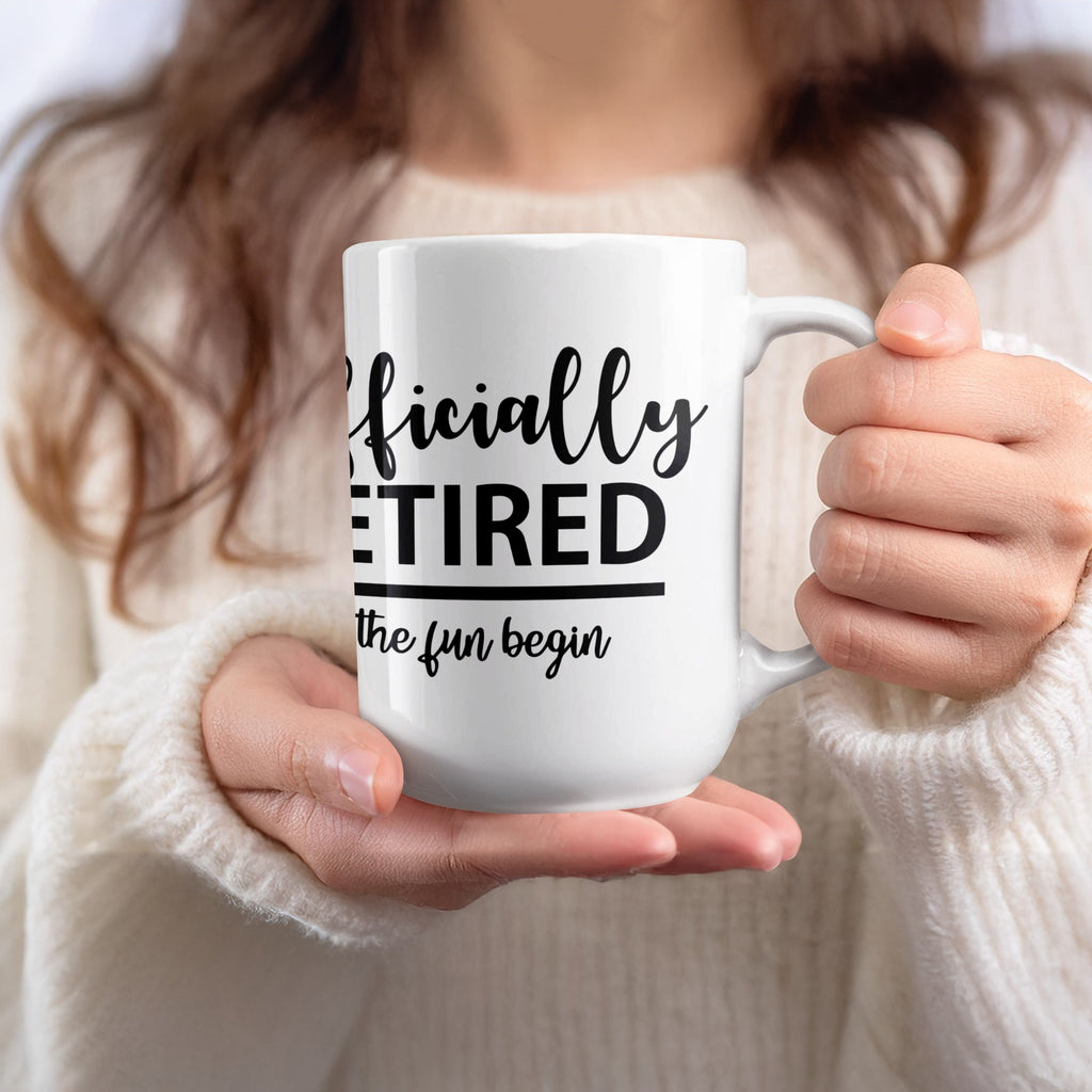 White mug with text "Officially RETIRED the fun begin" held by a person.