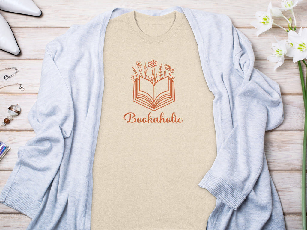 Tan t-shirt with orange book and flowers graphic and text "Bookaholic."