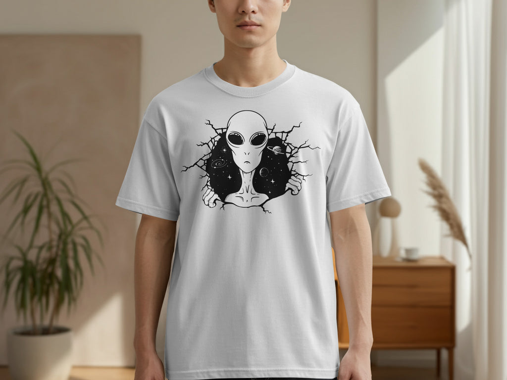 White t-shirt with a black graphic of an alien head and shoulders breaking through a cracked background with stars and planets.