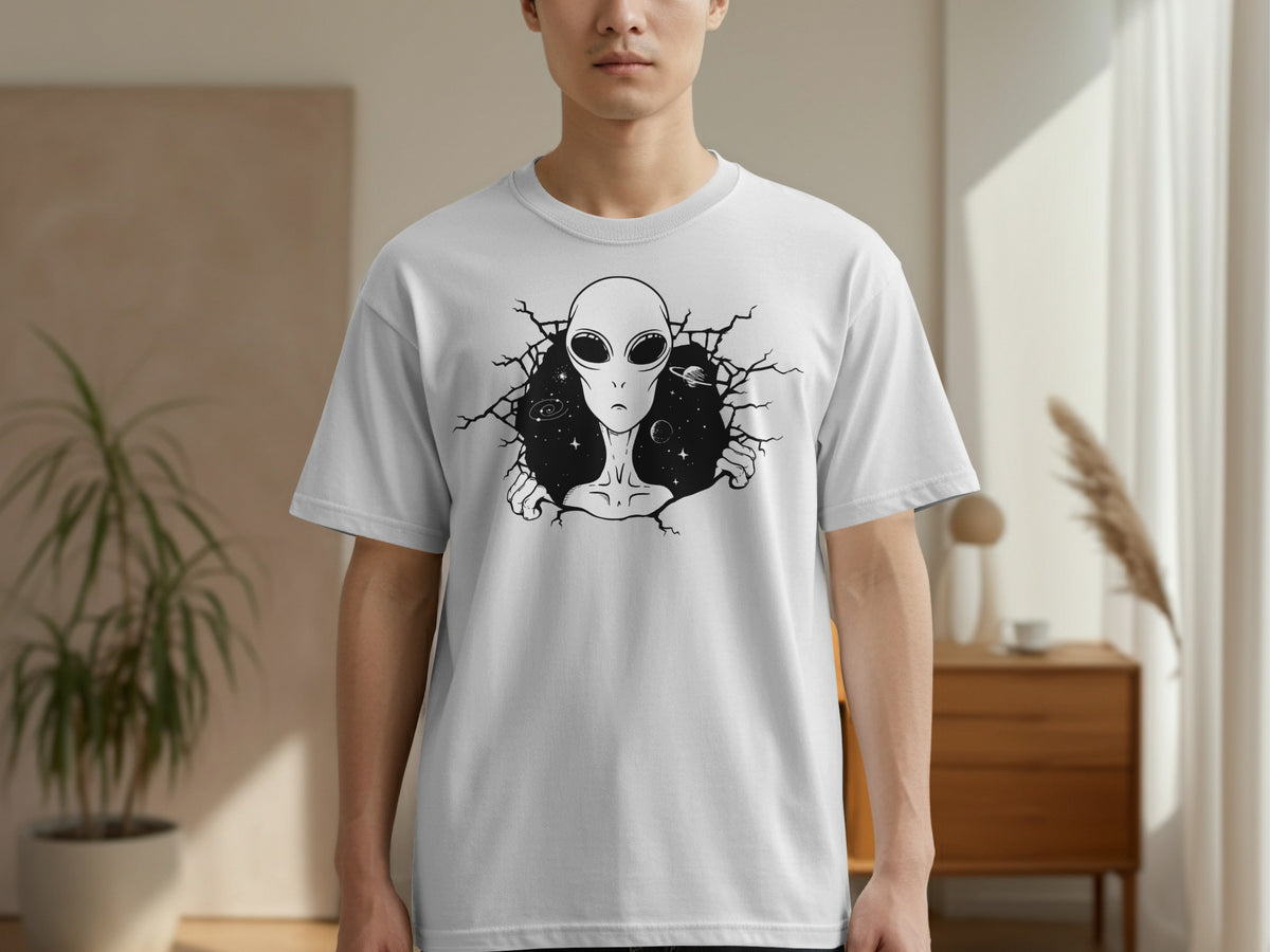 White t-shirt with a black graphic of an alien head and shoulders breaking through a cracked background with stars and planets.