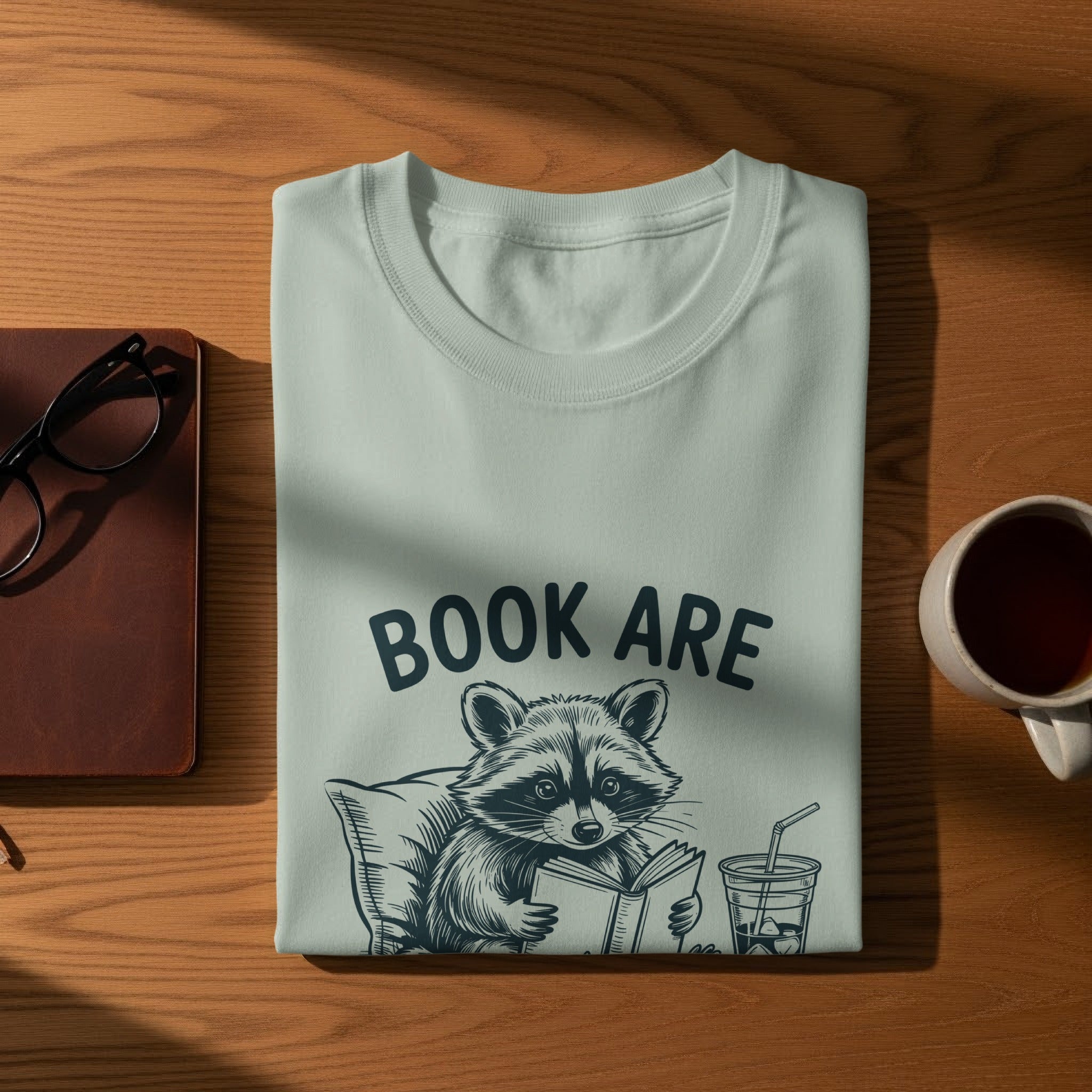 Light blue t-shirt with raccoon reading a book and text "BOOK ARE".
