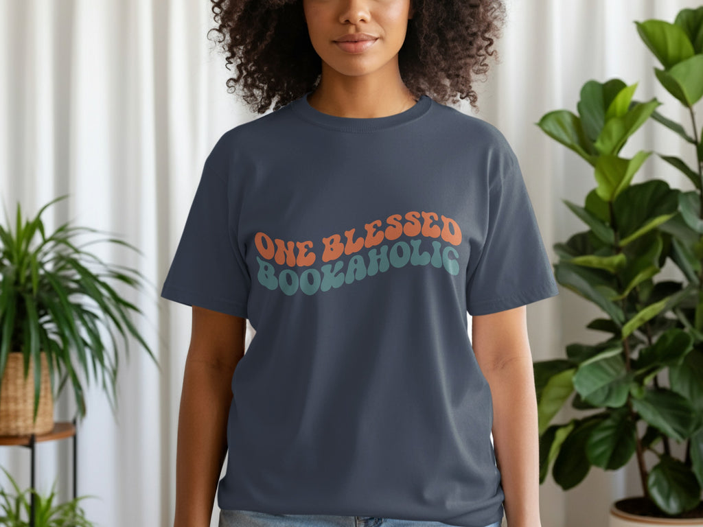 Dark blue t-shirt with "ONE BLESSED BOOKAHOLIC" text in orange and teal wavy font.