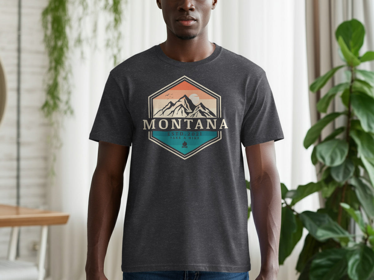 Dark t-shirt with a hexagonal graphic featuring mountains, sun, and "Montana Estd. 2021 Take a Hike."