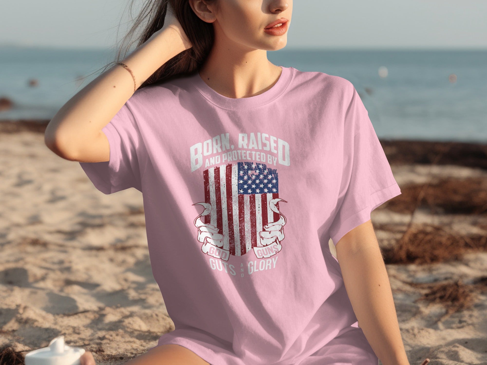 Pink t-shirt with American flag graphic and text: "Born, raised, and protected by God, guns, guts, and glory."