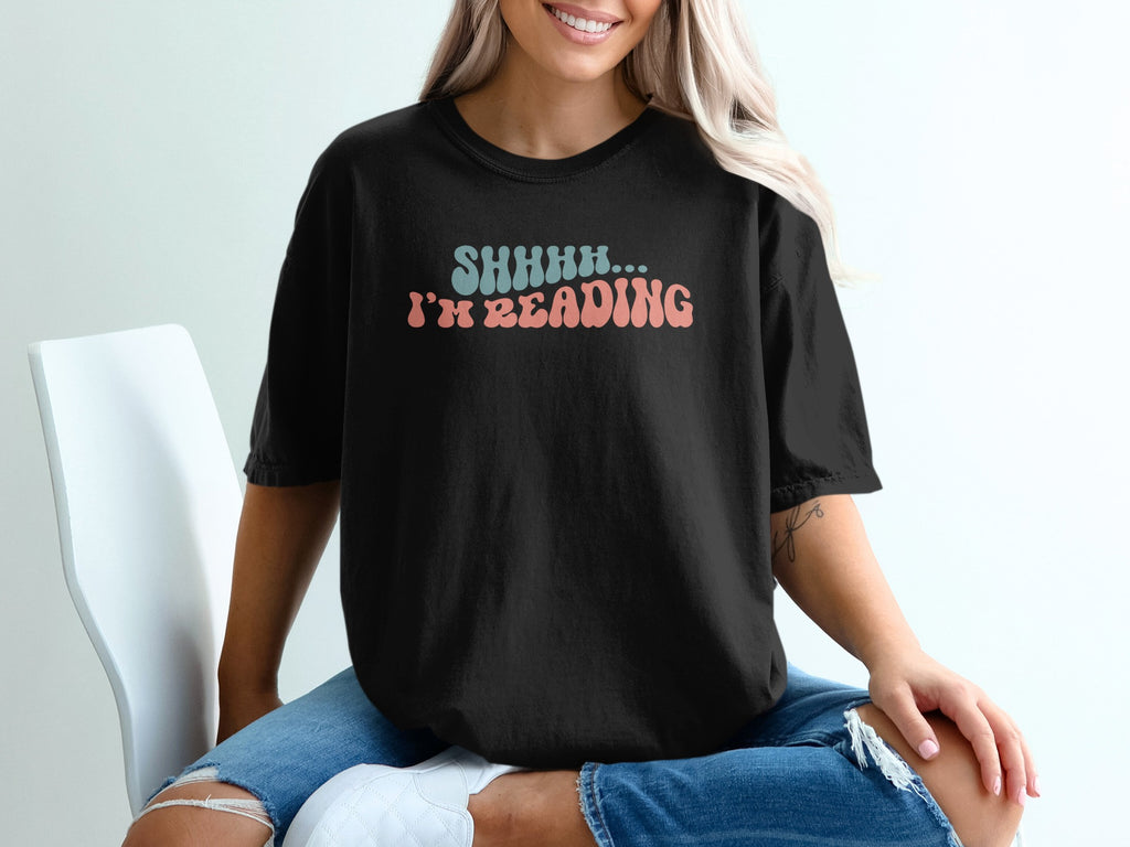 Black t-shirt with "SHHHH... I'M READING" text in wavy retro font.