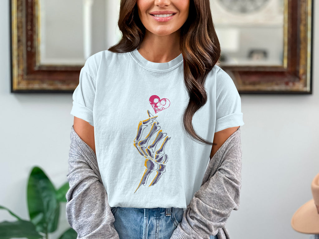 Skeleton hand making finger heart gesture below skull heart design on pale blue t-shirt.