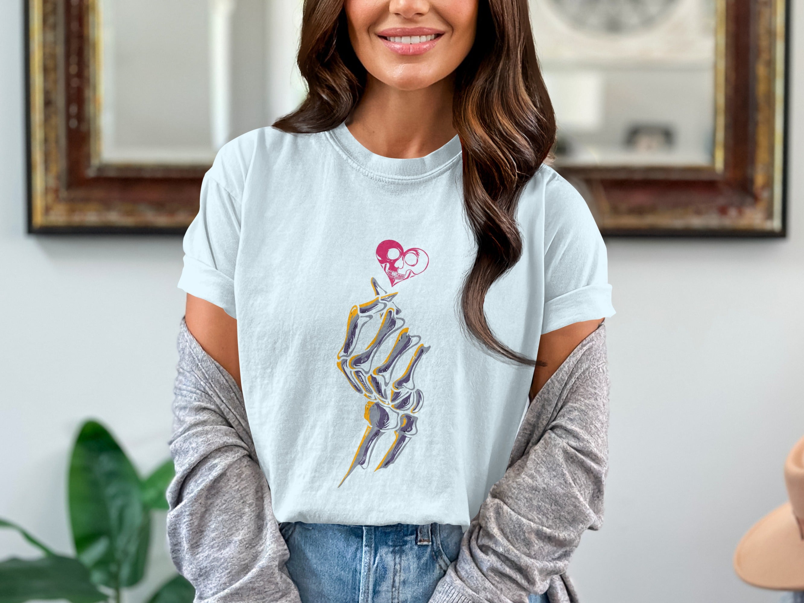 Skeleton hand making finger heart gesture below skull heart design on pale blue t-shirt.