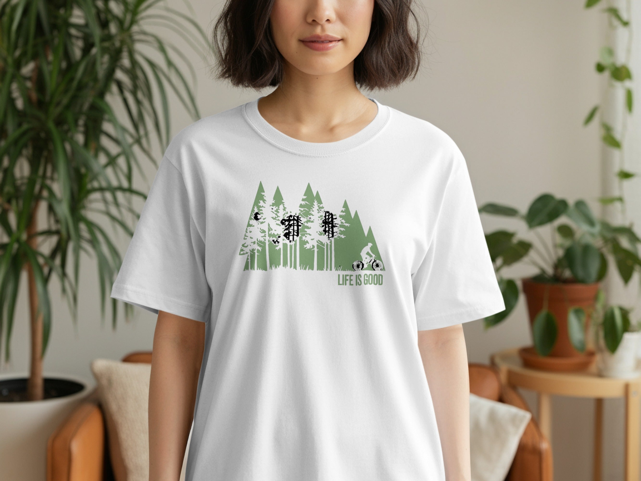 White t-shirt with green forest and cyclist graphic, text "LIFE IS GOOD".