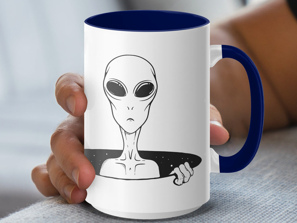 White mug with blue handle featuring a black and white alien peeking from a starry black void.
