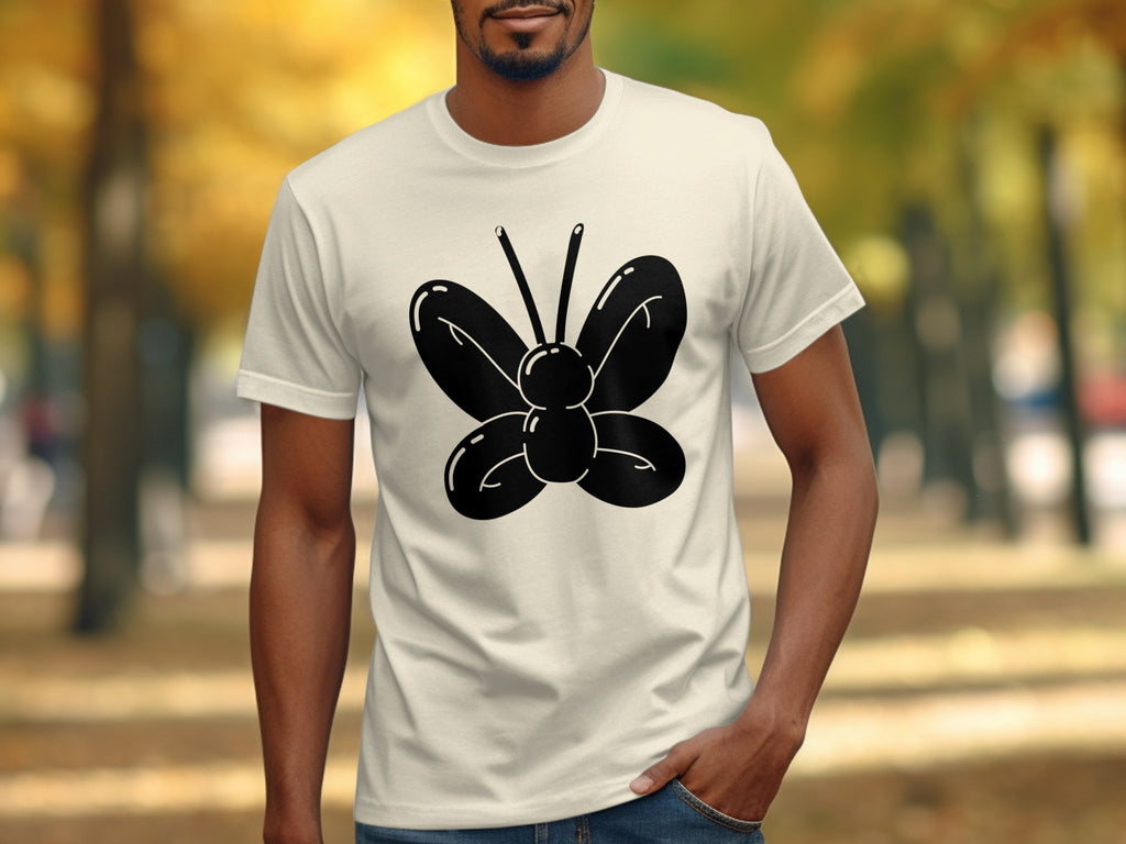 Cream t-shirt with black balloon butterfly graphic, outdoors with blurred autumn trees.