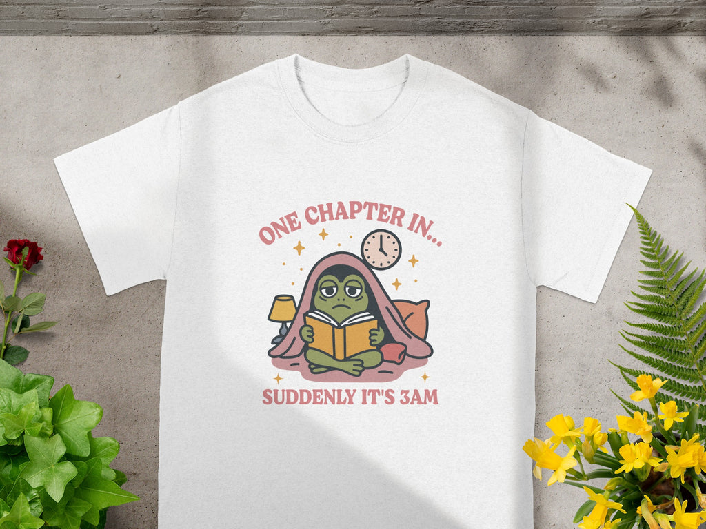 White t-shirt with frog reading a book under blankets and the text "One Chapter In... Suddenly It's 3 AM".