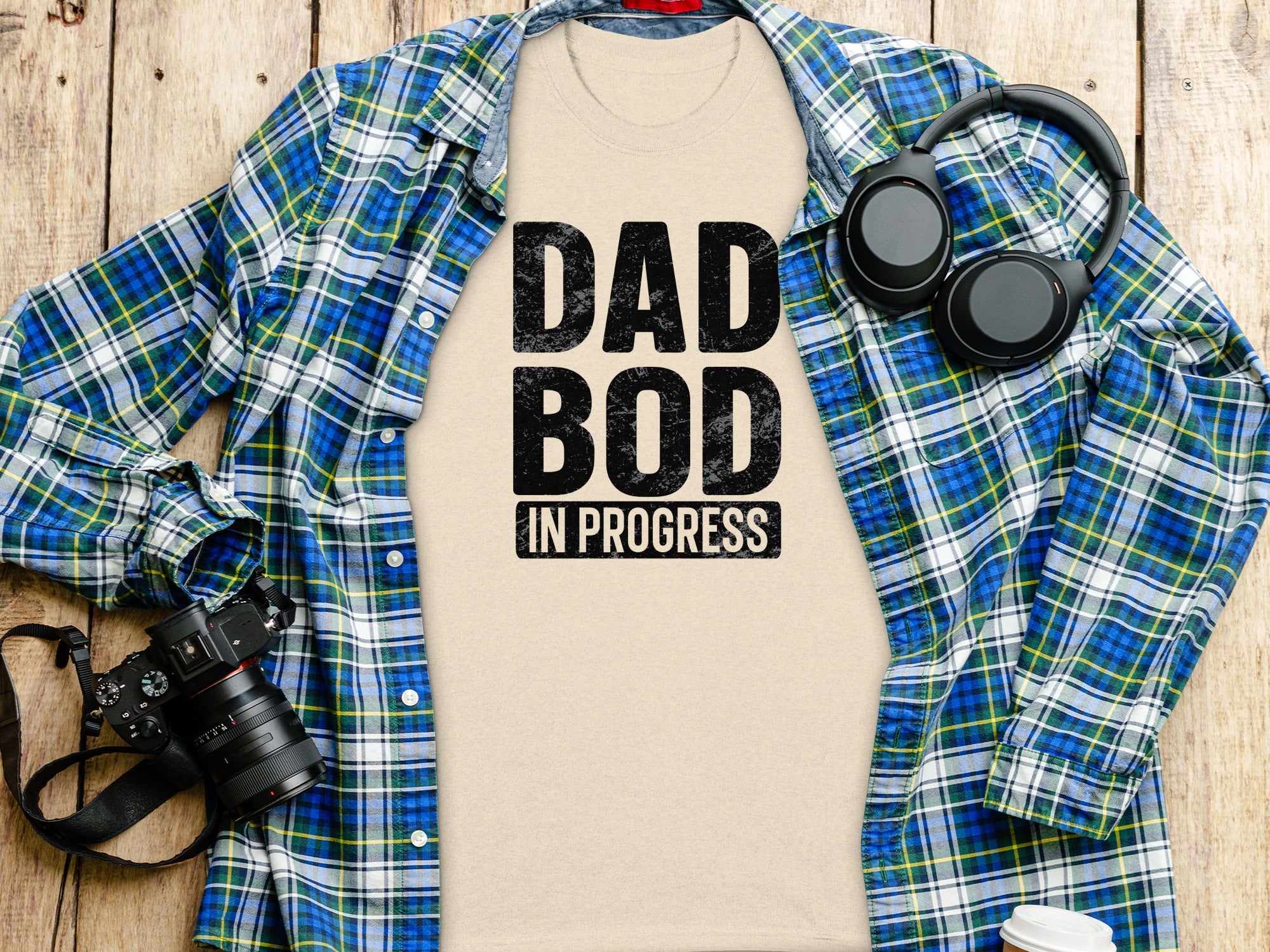 T-shirt with "DAD BOD IN PROGRESS" text, headphones, camera, and plaid shirt.