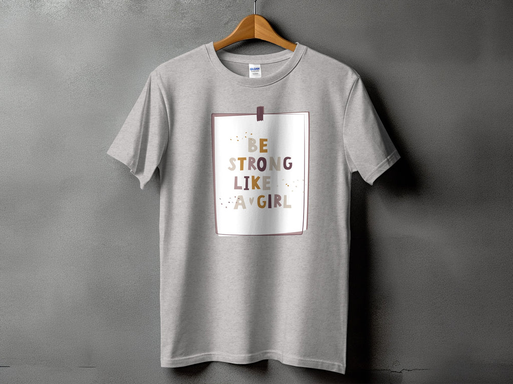 Grey t-shirt with "Be Strong Like A Girl" text in muted colors inside a framed border.