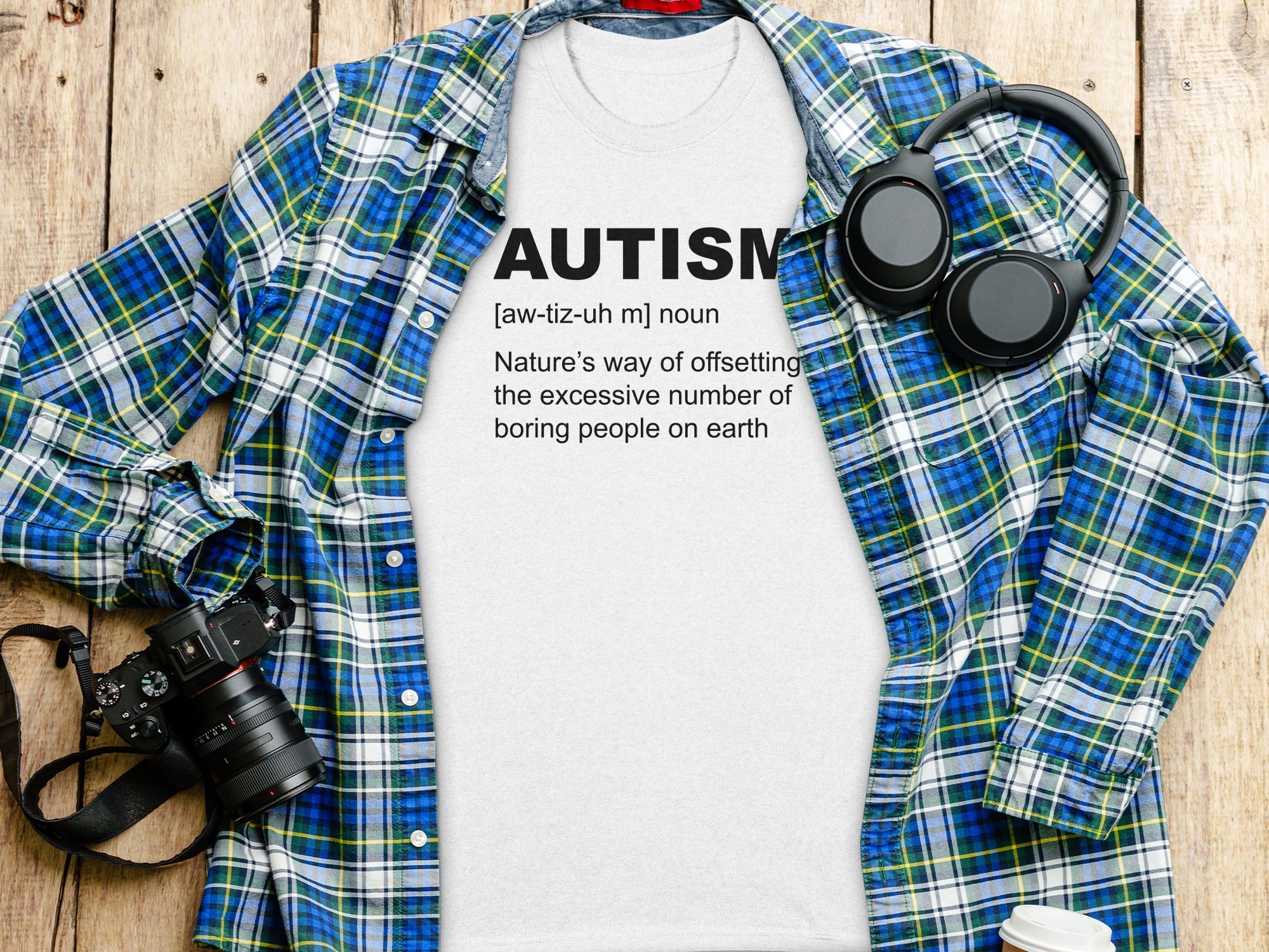 White t-shirt with "AUTISM" definition printed in black text, laid on a flannel shirt.