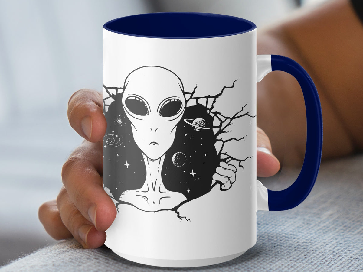 White mug with navy handle featuring an alien head emerging from a cracked background with stars and planets.