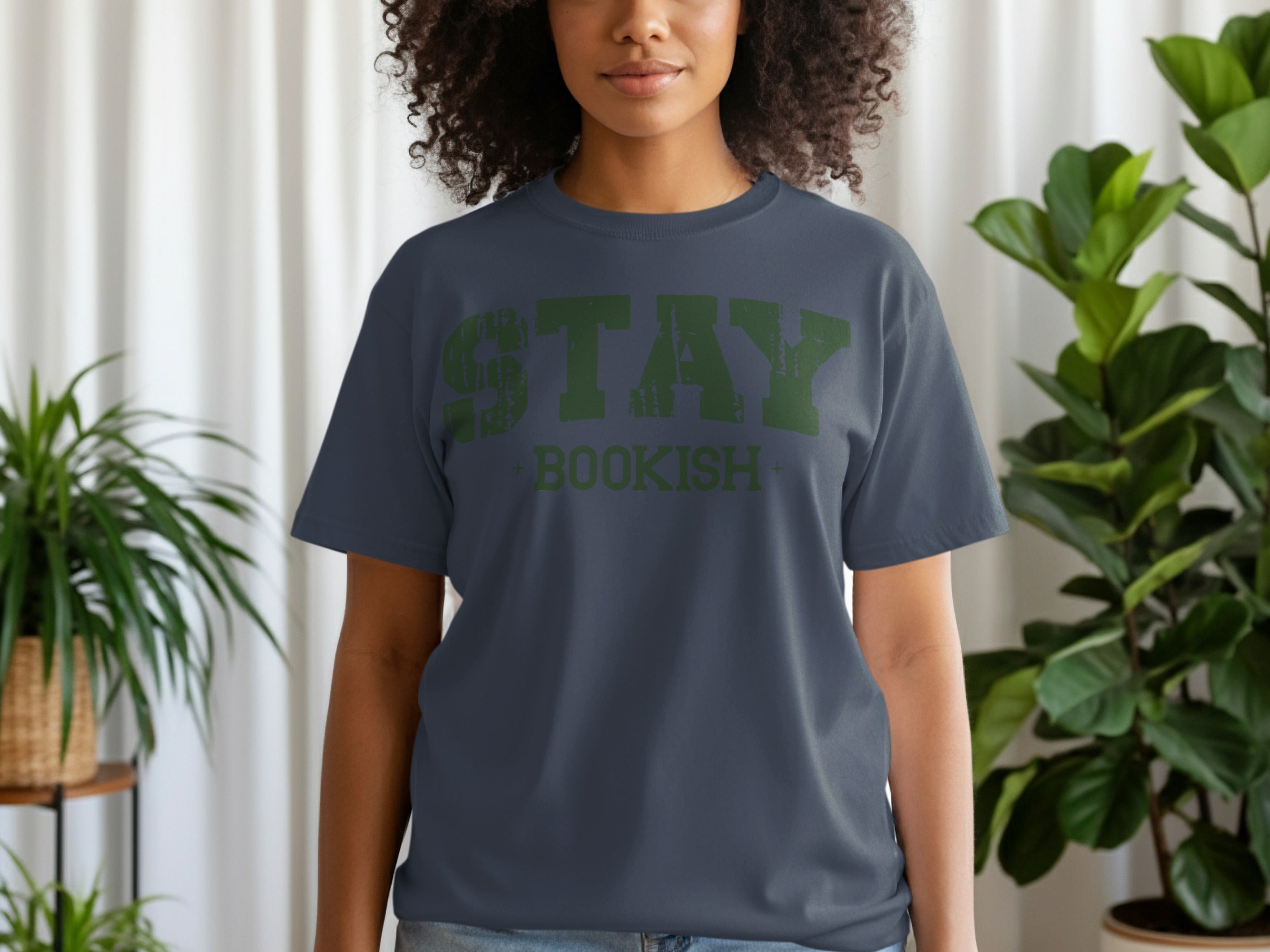 A woman wears a dark grey t-shirt with green distressed text "STAY BOOKISH".