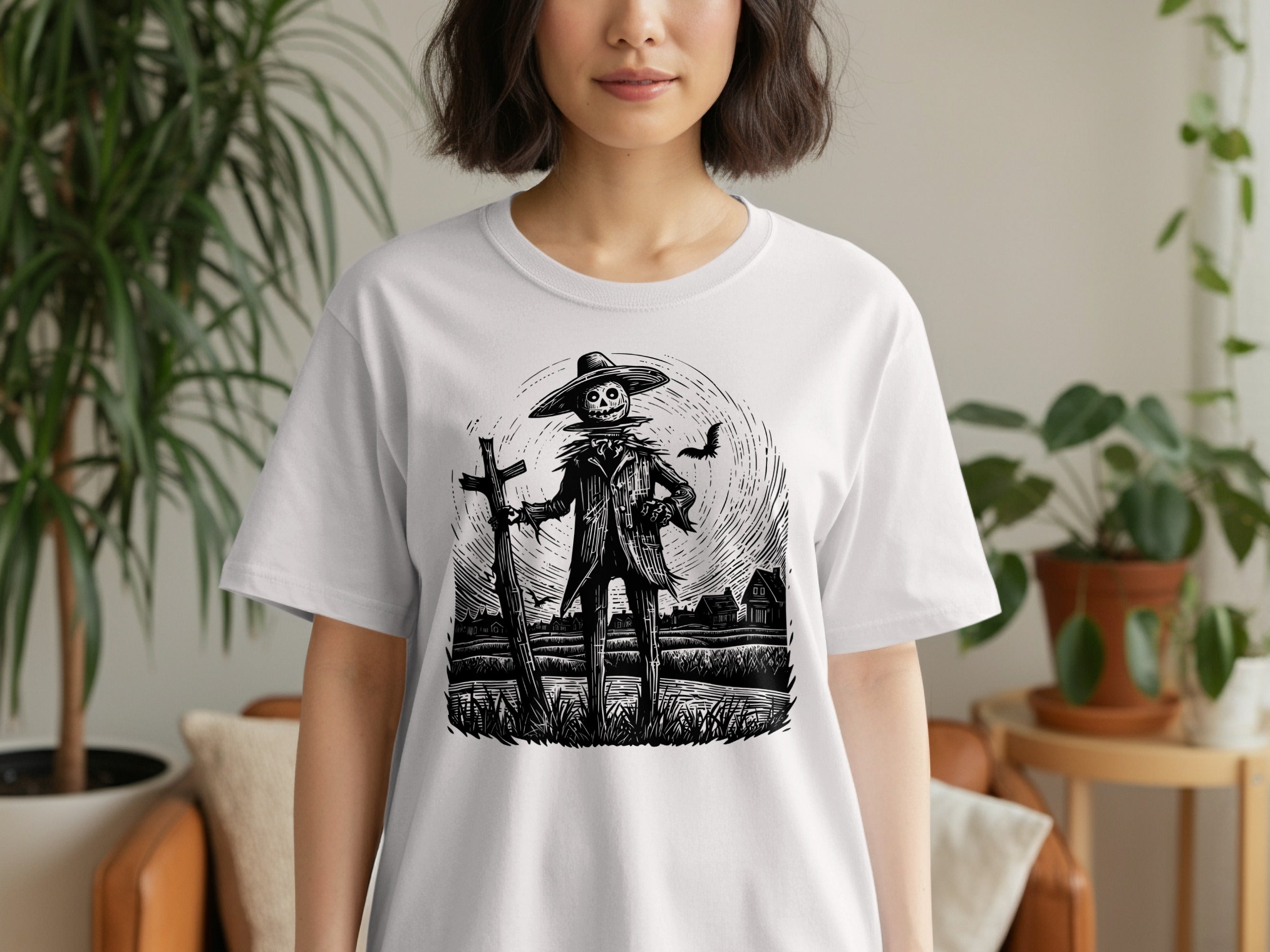 Scarecrow with moon, bat, and houses etching on a white t-shirt.