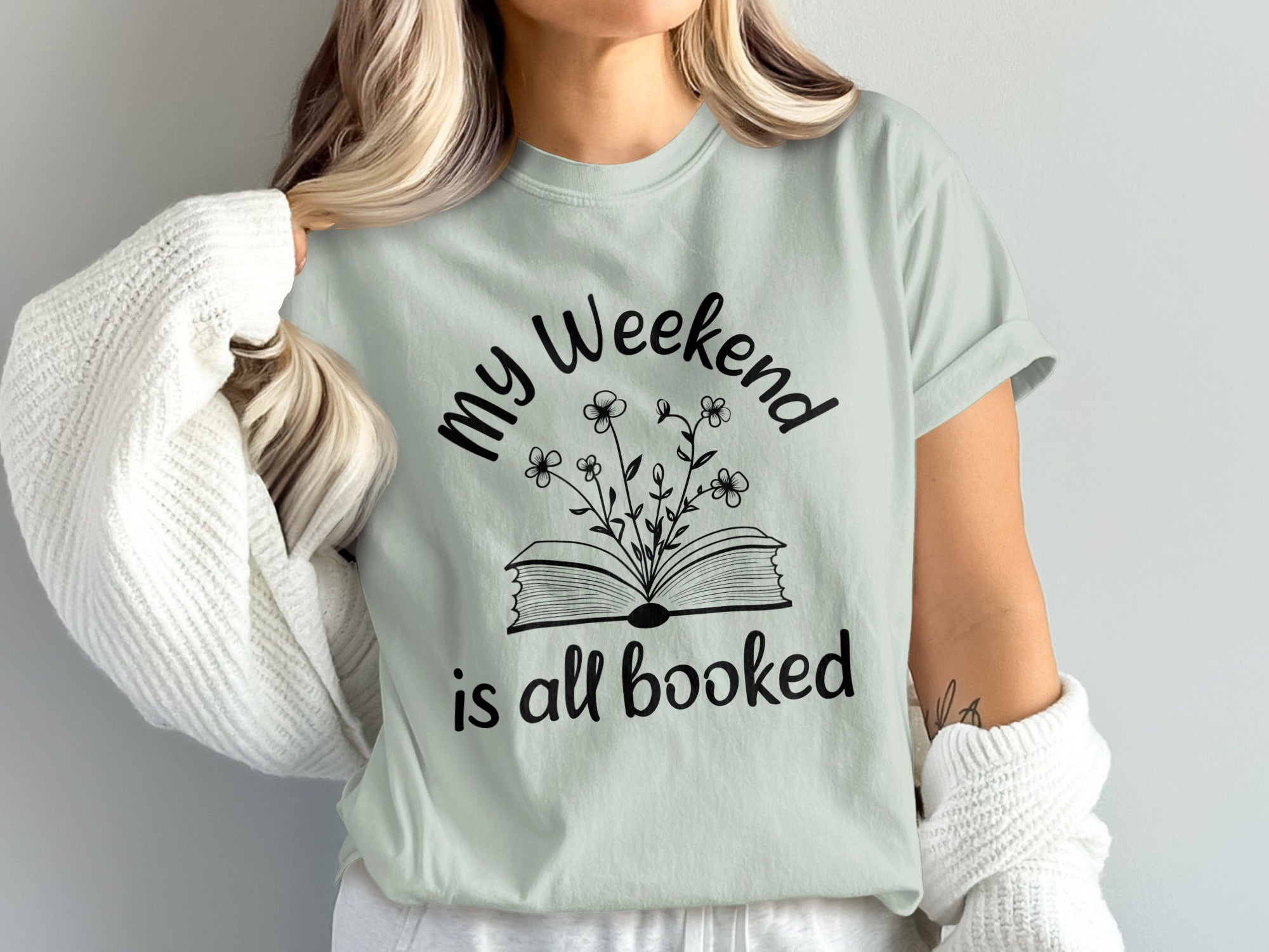 Light mint t-shirt with black text and illustration of open book with flowers.