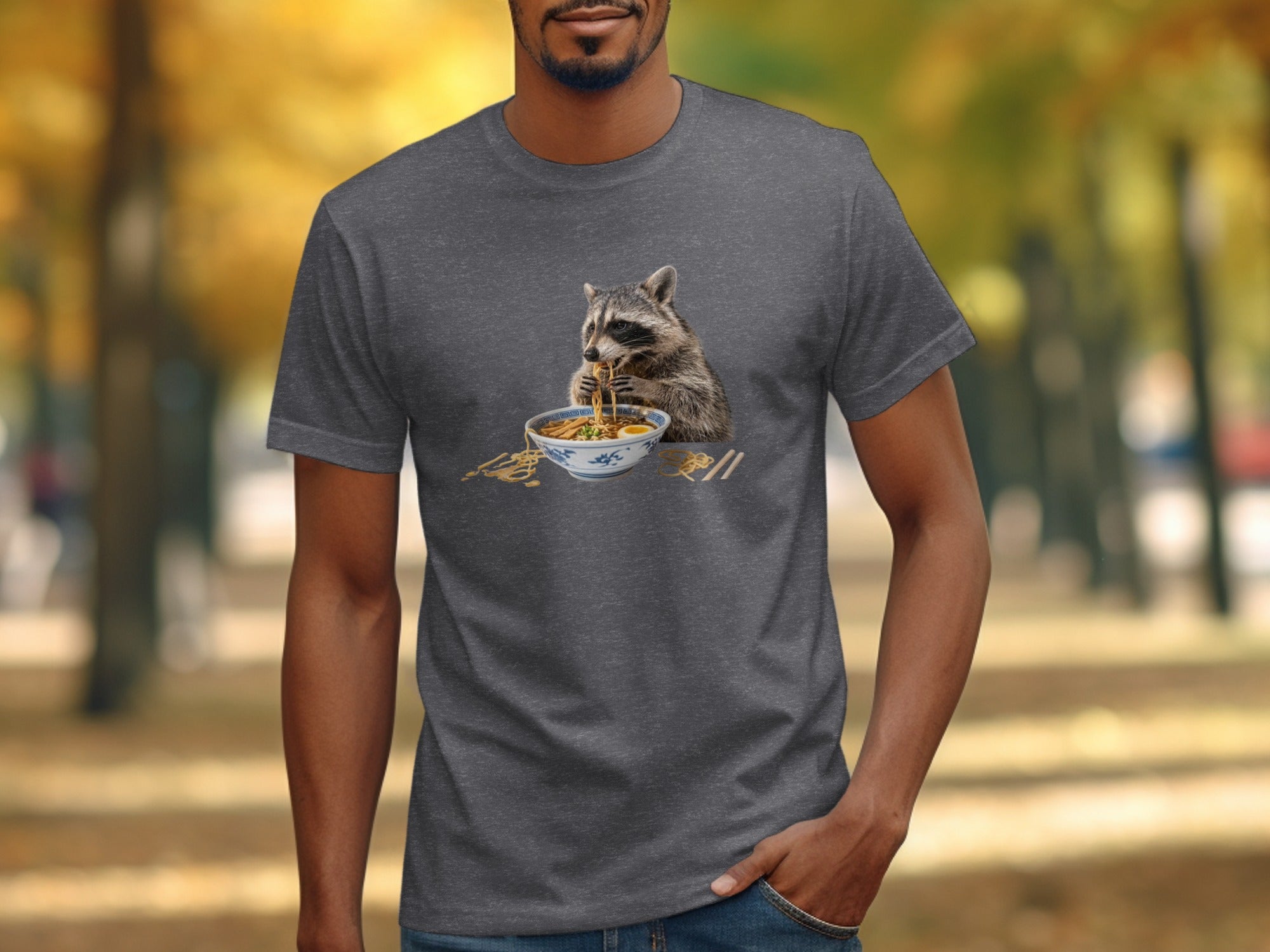Raccoon eating ramen with chopsticks on a gray t-shirt.