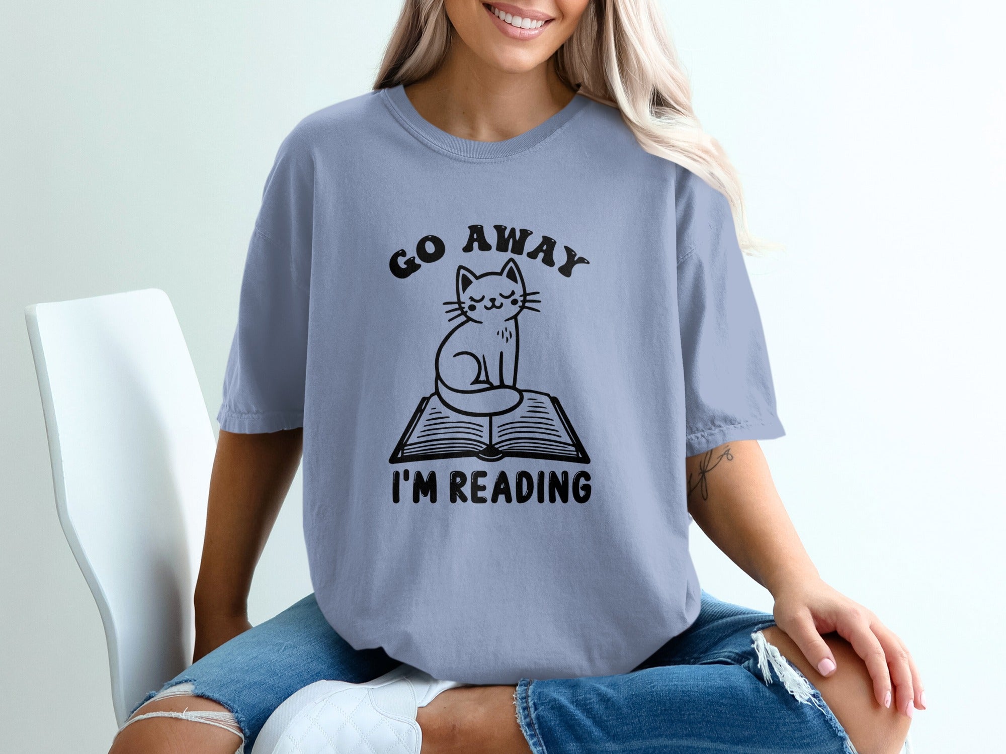 Blue t-shirt with black text and cat graphic reading "Go Away I'm Reading".