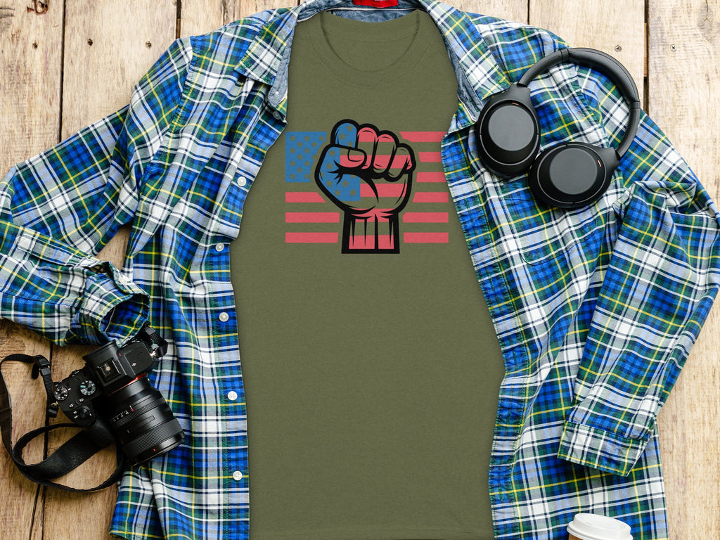 Olive green t-shirt with American flag fist graphic, plaid shirt, headphones, and camera.