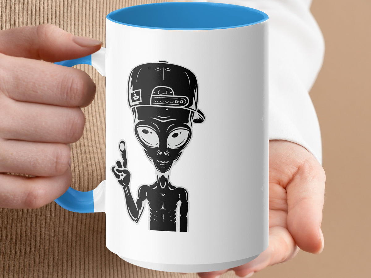 White mug with blue interior featuring a black alien in a baseball cap giving a peace sign.