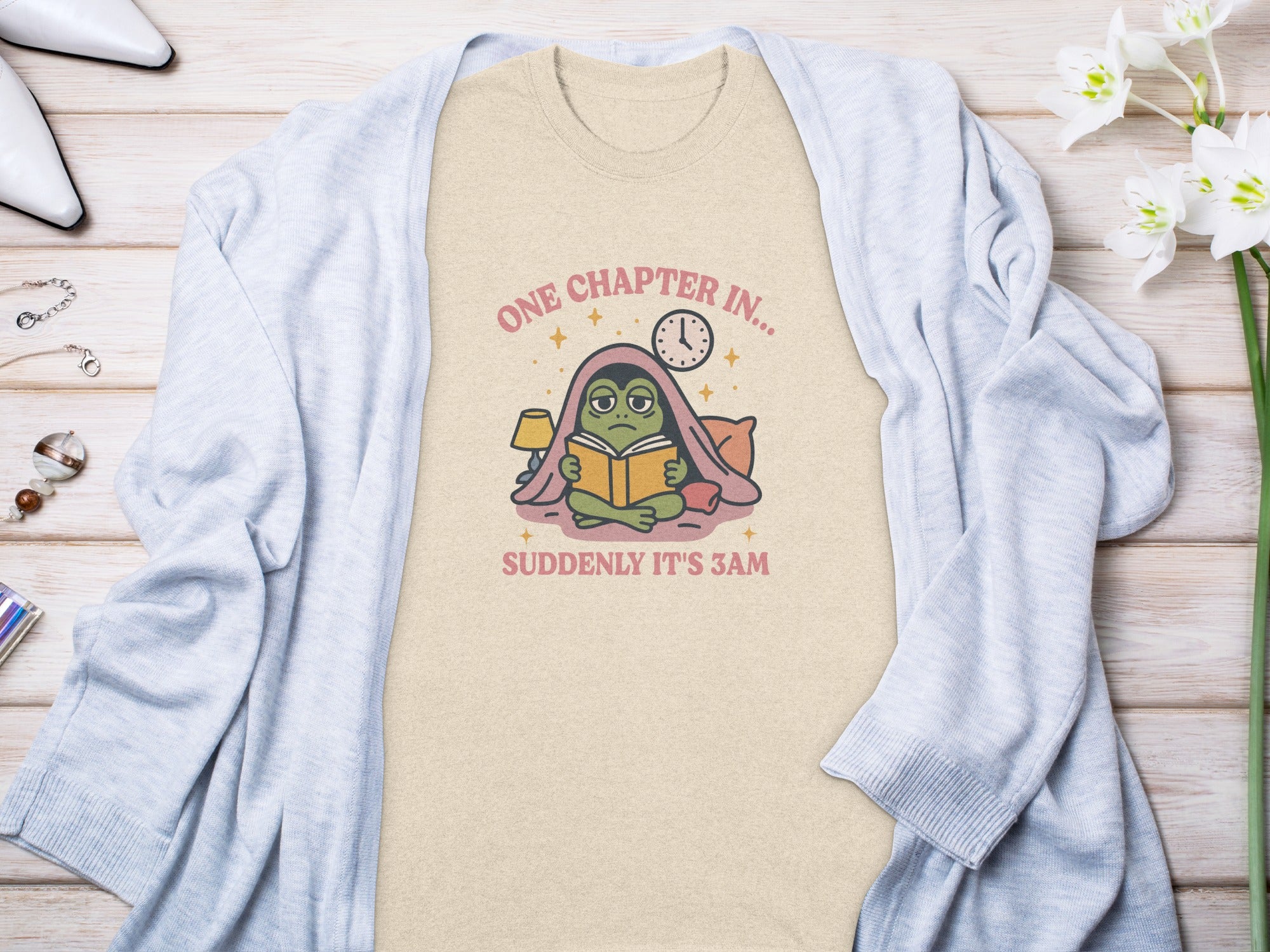 Beige t-shirt with frog reading in bed, "One Chapter In... Suddenly It's 3 AM".