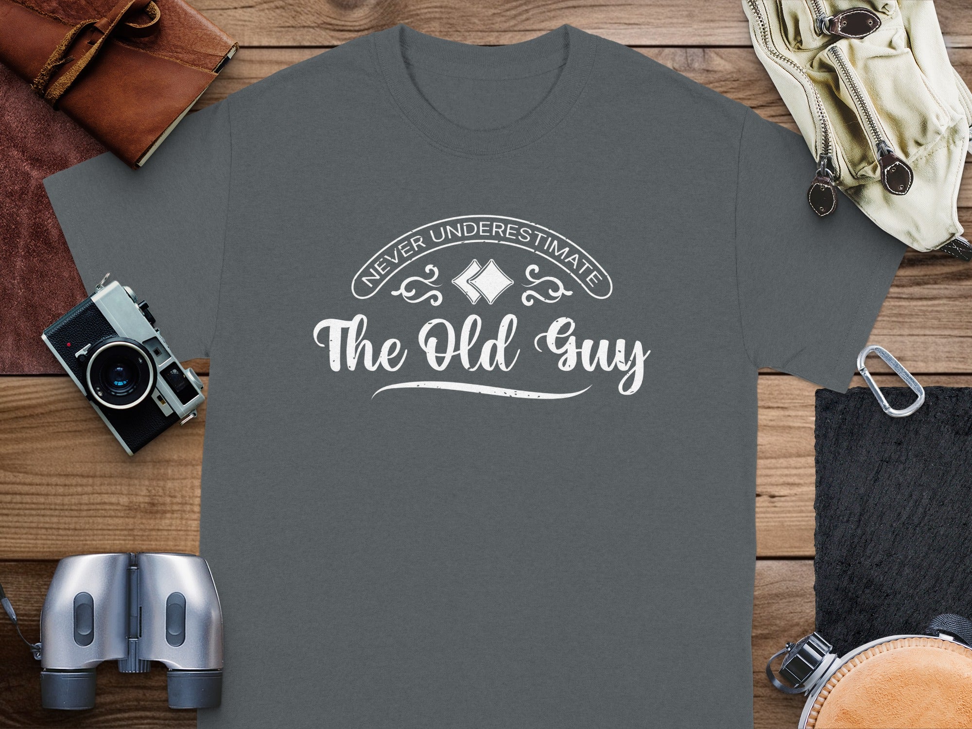 Dark gray t-shirt with white text "Never Underestimate The Old Guy".